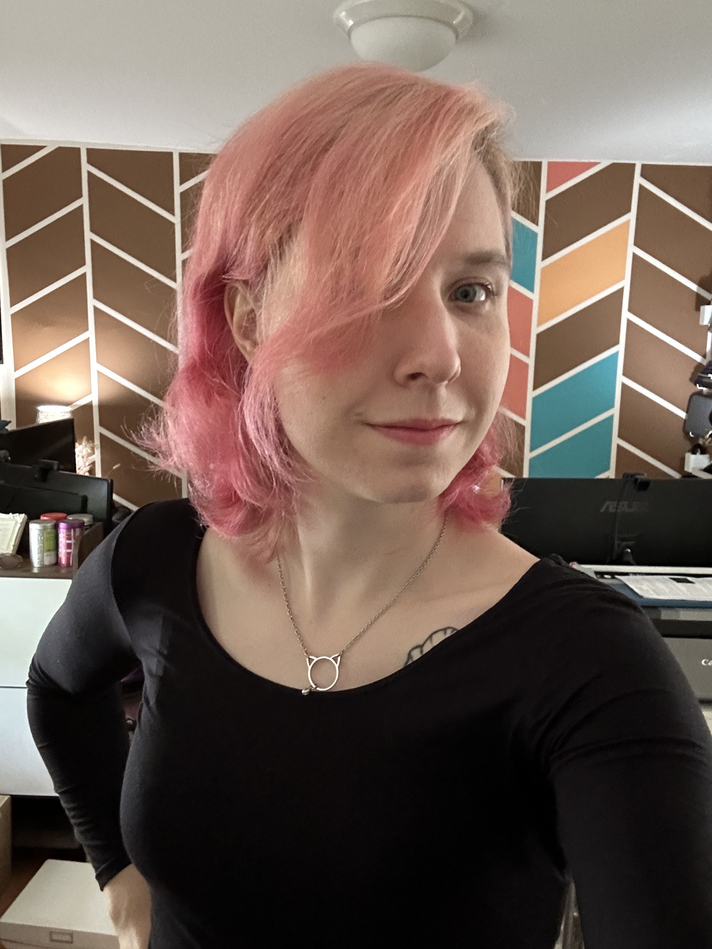 Lex Feathers, a woman with pink hair and black shirt. She has a slight smile.