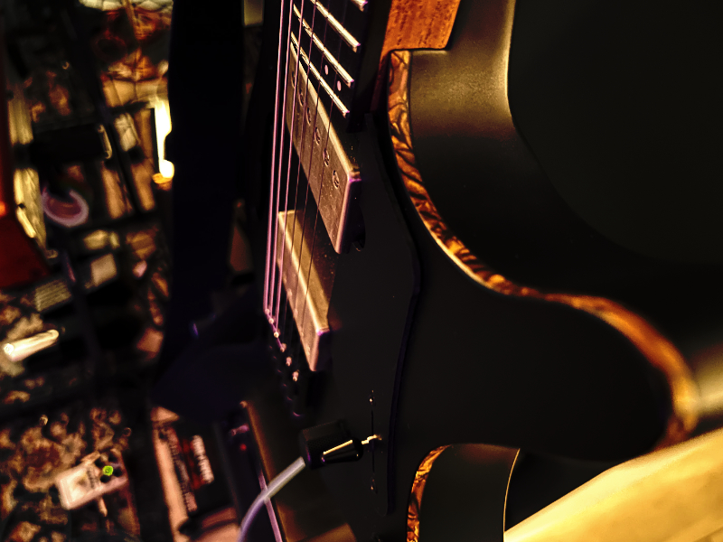 An electric guitar hanging on a wall above an amp and overdrive pedal